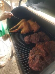 Image inside a smoker chamber, showing someone probe-testing a golden-brown turkey. Next to this are two briskets, each showing a dark bark.