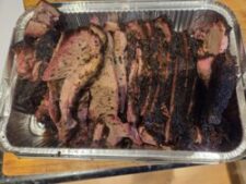 Image of a tray of sliced brisket. The meat shows smoke ring and a dark bark, and the juices are visible.